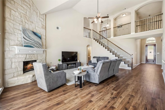 living area featuring stairs, wood finished floors, a ceiling fan, high vaulted ceiling, and a fireplace