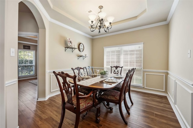 dining space featuring a chandelier, a raised ceiling, dark wood-style flooring, wainscoting, and arched walkways