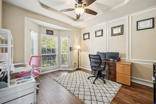 office area with a raised ceiling, ceiling fan, wood finished floors, and a decorative wall