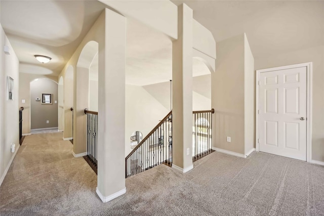 corridor featuring an upstairs landing, carpet, arched walkways, and baseboards