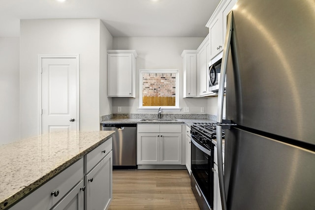377 Tejas Trl, Waller, TX 77484 - kitchen with stainless steel appliances, a sink, light wood-style floors, light stone countertops, and white cabinetry