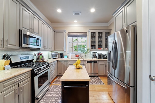 3219 N Pemberton Circle Dr, Houston, TX 77025 - kitchen featuring appliances with stainless steel finishes, crown molding, gray cabinetry, glass insert cabinets, and backsplash