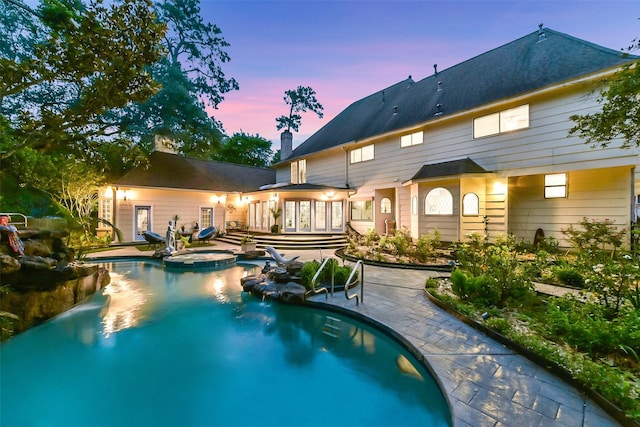 3230 Ivy Falls Dr, Houston, TX 77068 - back of house at dusk featuring a patio, a chimney, a pool with connected hot tub, and french doors