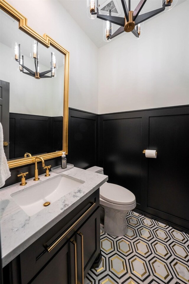 1924 Boulder Ridge Dr, Conroe, TX 77304 - bathroom with a chandelier, vanity, toilet, wainscoting, and a decorative wall