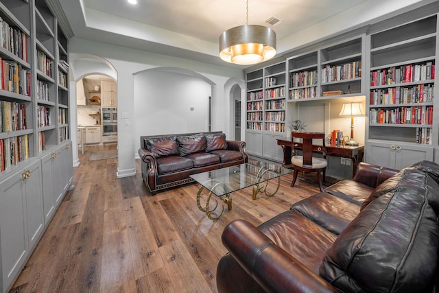 1924 Boulder Ridge Dr, Conroe, TX 77304 - living area with arched walkways, wood finished floors, wall of books, built in features, and a raised ceiling