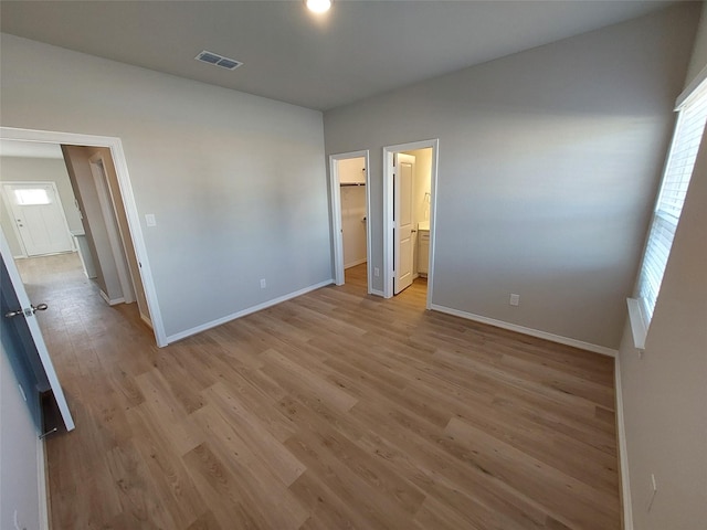 unfurnished bedroom with baseboards, multiple windows, light wood-style floors, and a walk in closet