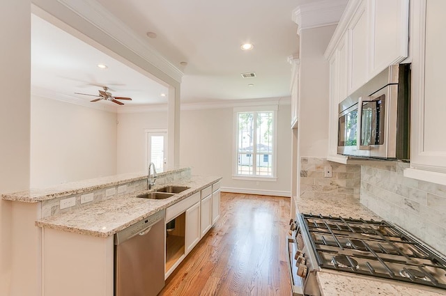 kitchen featuring appliances with stainless steel finishes, a sink, ornamental molding, white cabinets, and tasteful backsplash