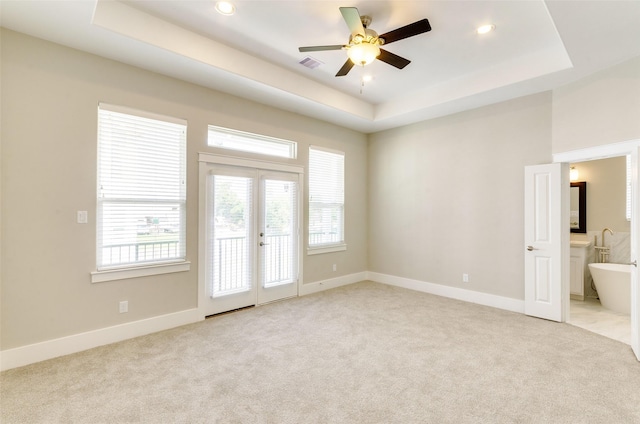 empty room featuring a tray ceiling, ceiling fan, french doors, light carpet, and baseboards