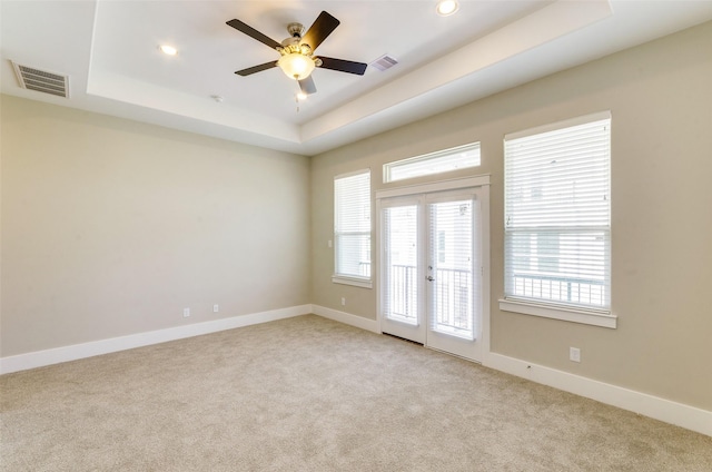 unfurnished room featuring light carpet, a tray ceiling, french doors, a ceiling fan, and baseboards