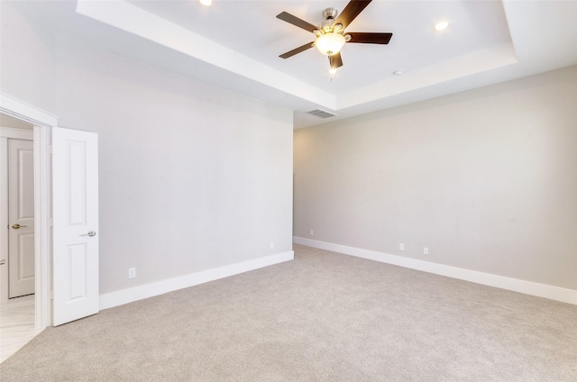spare room with a tray ceiling, light colored carpet, a ceiling fan, recessed lighting, and baseboards