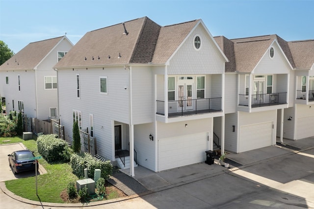 view of front facade featuring an attached garage, driveway, fence, a balcony, and roof with shingles