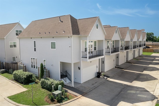 back of property featuring a shingled roof, fence, driveway, a balcony, and a residential view