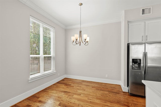 unfurnished dining area featuring crown molding, a chandelier, baseboards, and light wood finished floors