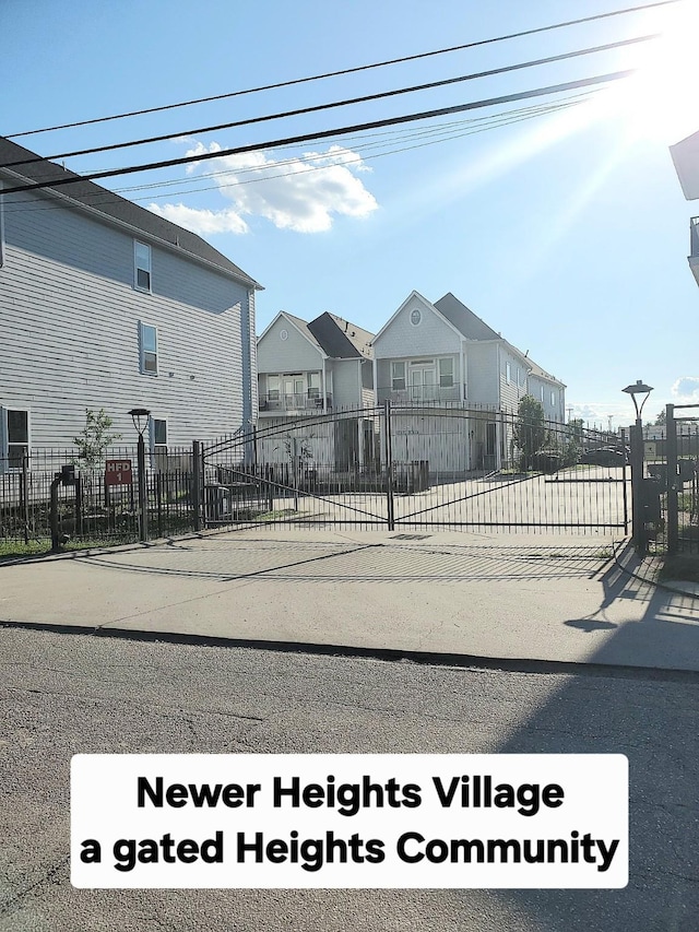 view of asphalt street with street lighting, a gated entry, and a residential view