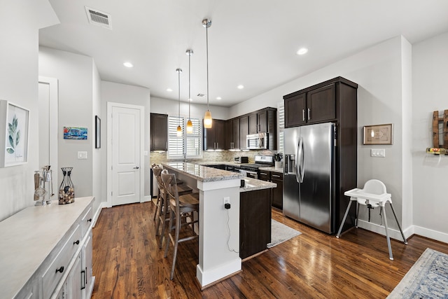 kitchen featuring stainless steel appliances, dark brown cabinets, a breakfast bar area, a kitchen island, and dark wood-type flooring
