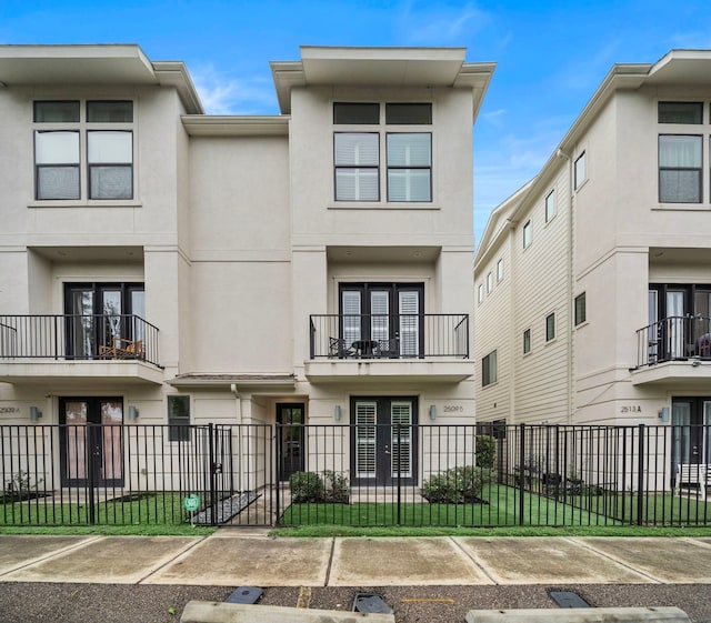 townhome / multi-family property featuring stucco siding, french doors, uncovered parking, a fenced front yard, and a balcony