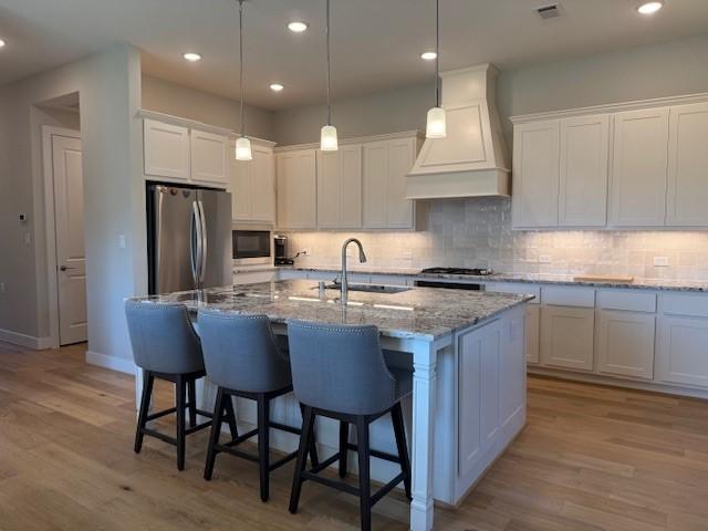 18714 Sweetwater Springs Dr, Cypress, TX 77433 - kitchen featuring custom exhaust hood, stainless steel appliances, a sink, light wood-style flooring, and white cabinetry