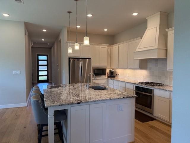 18714 Sweetwater Springs Dr, Cypress, TX 77433 - kitchen featuring stainless steel appliances, a sink, light wood-type flooring, premium range hood, and decorative backsplash