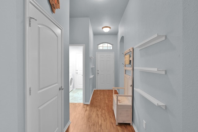 foyer entrance featuring washer / dryer, light wood finished floors, arched walkways, and baseboards
