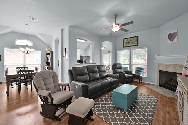 living room featuring a ceiling fan, a chandelier, a tiled fireplace, lofted ceiling, and plenty of natural light