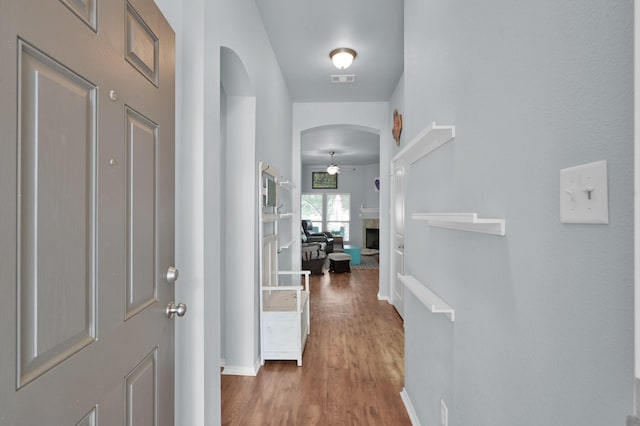 hall featuring arched walkways, baseboards, and wood finished floors