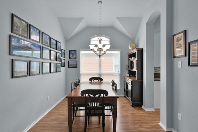 dining area with a chandelier, wood finished floors, baseboards, and lofted ceiling