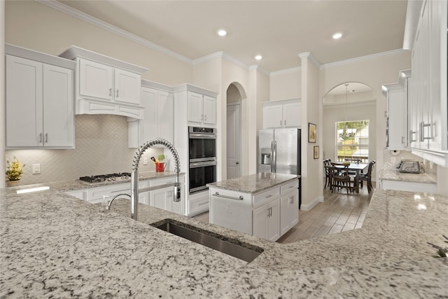 23440 Yaupon Hills Dr, New Caney, TX 77357 - kitchen featuring arched walkways, stainless steel appliances, light stone counters, white cabinets, and tasteful backsplash