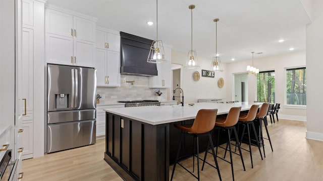 7321 Ponderosa Dr, Magnolia, TX 77354 - kitchen with stainless steel refrigerator with ice dispenser, premium range hood, tasteful backsplash, light countertops, and light wood finished floors