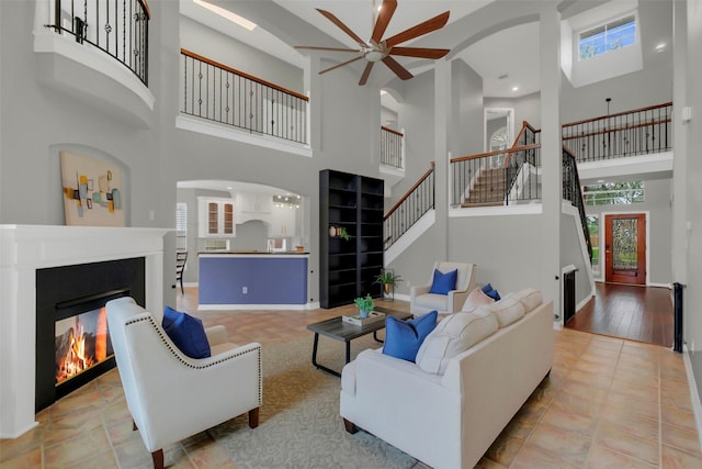 9619 Silver Birch Ct, Missouri City, TX 77459 - living area featuring a lit fireplace, a high ceiling, stairs, arched walkways, and ceiling fan