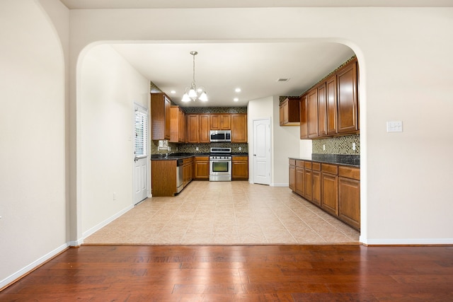 506 Stream Mill Ln, Katy, TX 77494 - kitchen featuring appliances with stainless steel finishes, dark countertops, brown cabinets, a chandelier, and decorative backsplash