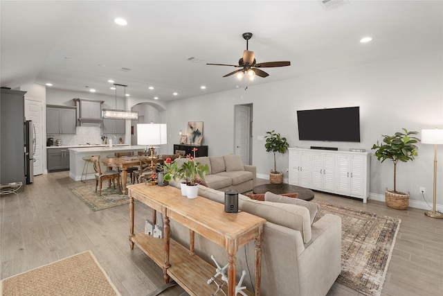 living room with ceiling fan, vaulted ceiling, light wood-type flooring, recessed lighting, and baseboards
