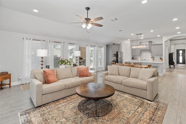 living room with arched walkways, ceiling fan, recessed lighting, light wood-type flooring, and lofted ceiling