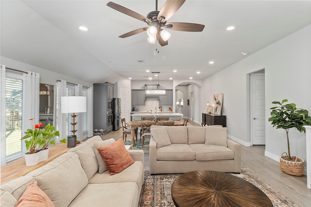 living room featuring arched walkways, ceiling fan, light wood finished floors, baseboards, and recessed lighting