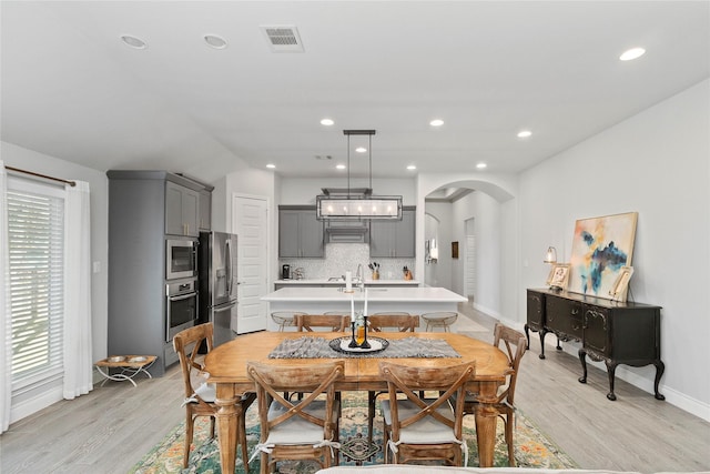 dining space featuring baseboards, light wood-style flooring, arched walkways, plenty of natural light, and recessed lighting