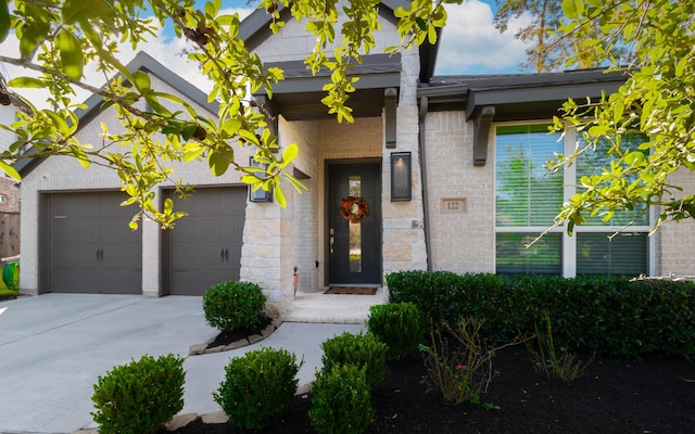 entrance to property featuring concrete driveway, an attached garage, and stone siding