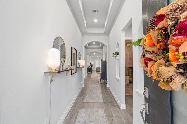 corridor featuring arched walkways, recessed lighting, baseboards, and light wood-type flooring