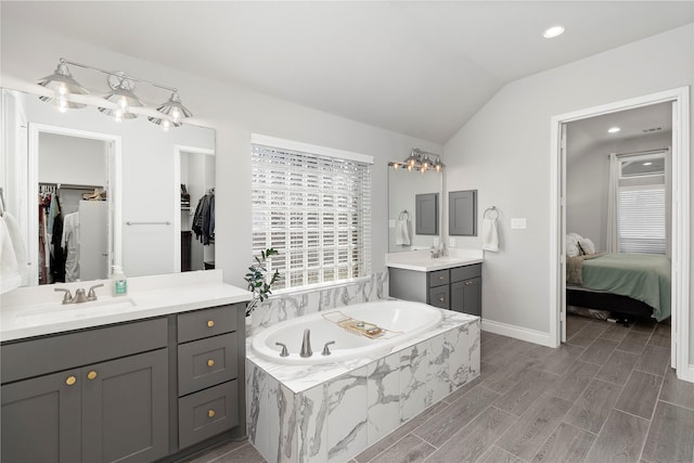 ensuite bathroom featuring vaulted ceiling, a spacious closet, a bath, two vanities, and recessed lighting