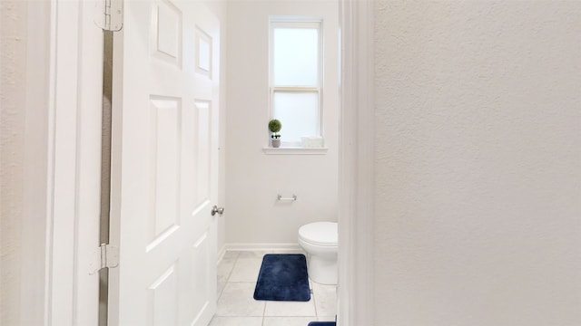 bathroom with tile patterned flooring, toilet, a textured wall, and baseboards