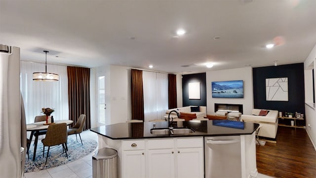 kitchen featuring appliances with stainless steel finishes, a sink, open floor plan, dark countertops, and a center island with sink