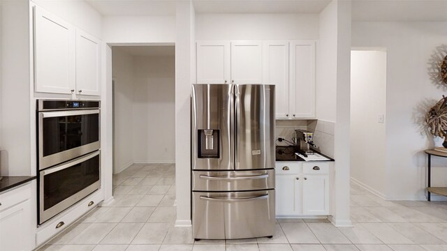 kitchen featuring appliances with stainless steel finishes, dark countertops, light tile patterned floors, white cabinets, and backsplash