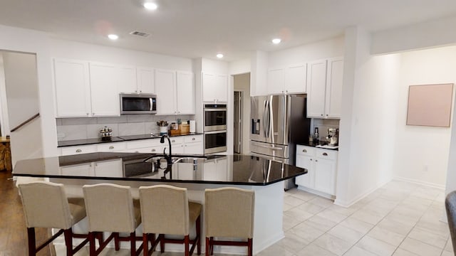kitchen with stainless steel appliances, a breakfast bar, dark countertops, decorative backsplash, and a sink