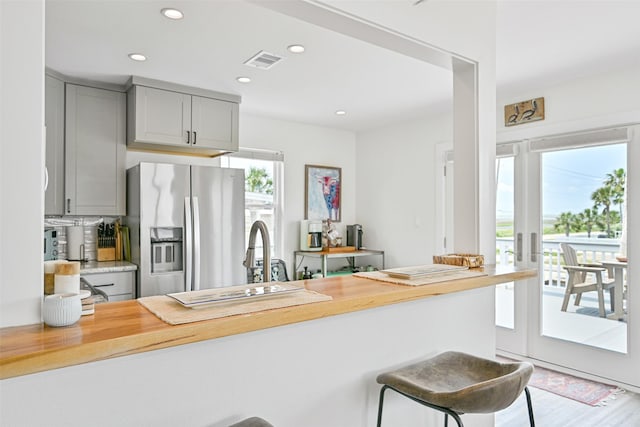 16716 Tahiti Way, Galveston, TX 77554 - kitchen with stainless steel fridge, gray cabinets, a kitchen bar, wood counters, and recessed lighting