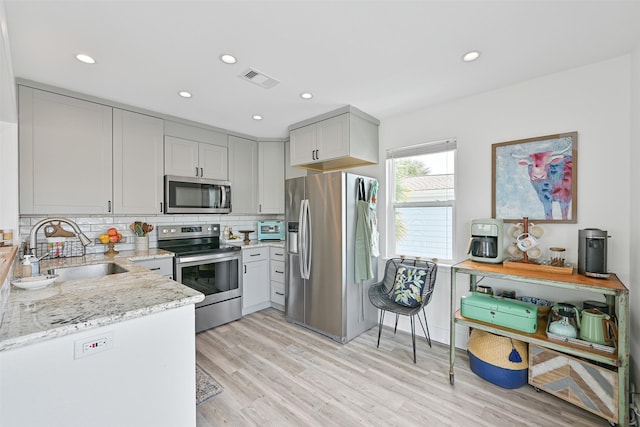 16716 Tahiti Way, Galveston, TX 77554 - kitchen featuring appliances with stainless steel finishes, a sink, light stone counters, decorative backsplash, and light wood-style floors