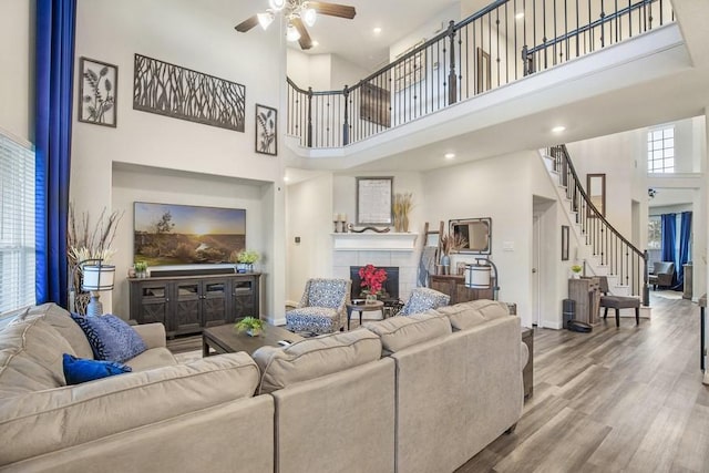 13814 Russell Ct, Mont Belvieu, TX 77523 - living room featuring a high ceiling, ceiling fan, a tiled fireplace, wood finished floors, and stairs