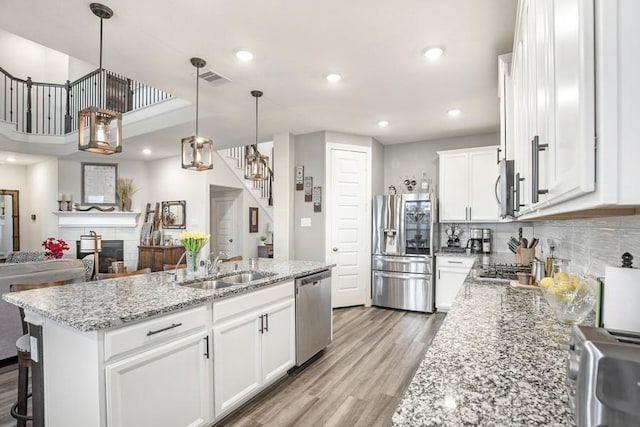 13814 Russell Ct, Mont Belvieu, TX 77523 - kitchen featuring stainless steel appliances, a sink, light wood-style flooring, white cabinetry, and decorative light fixtures