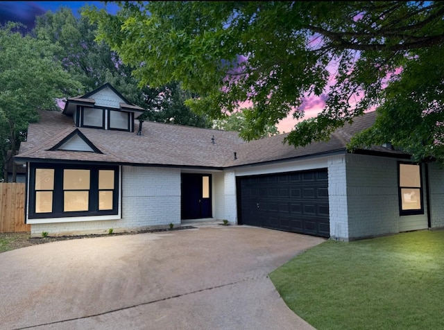 view of front of house with an attached garage, roof with shingles, brick siding, and driveway