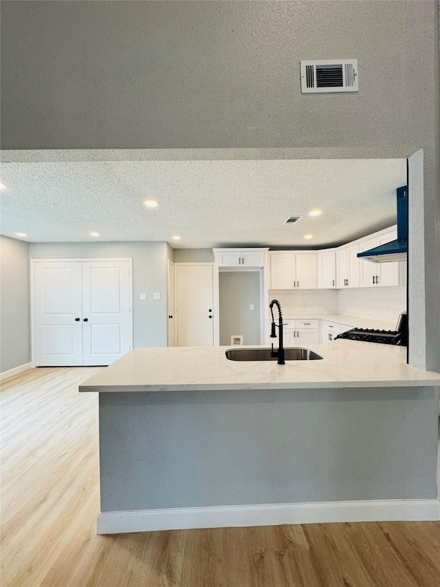 kitchen featuring a sink, wall chimney exhaust hood, light wood-style floors, black gas range, and light countertops