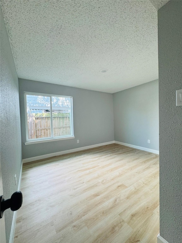 empty room featuring a textured wall, wood finished floors, a textured ceiling, and baseboards
