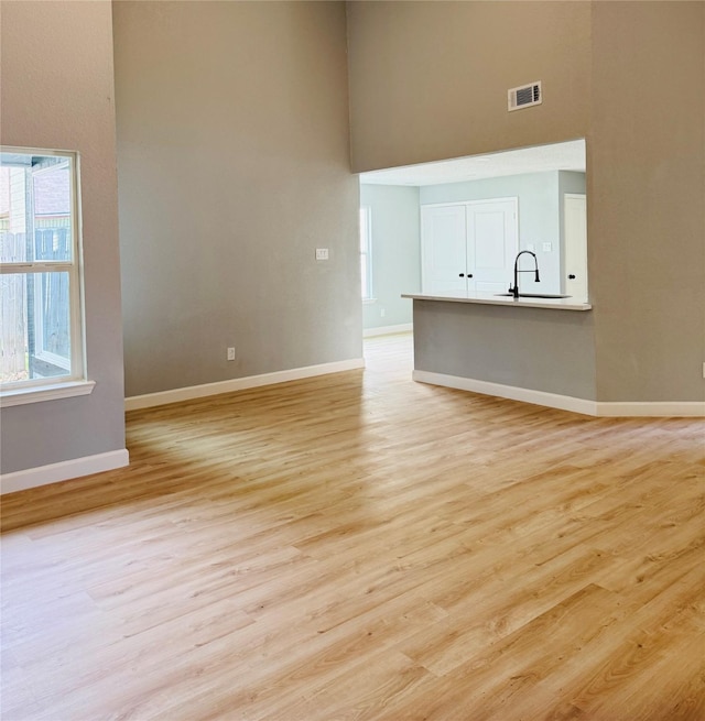 empty room with a high ceiling, a sink, baseboards, and light wood-style flooring