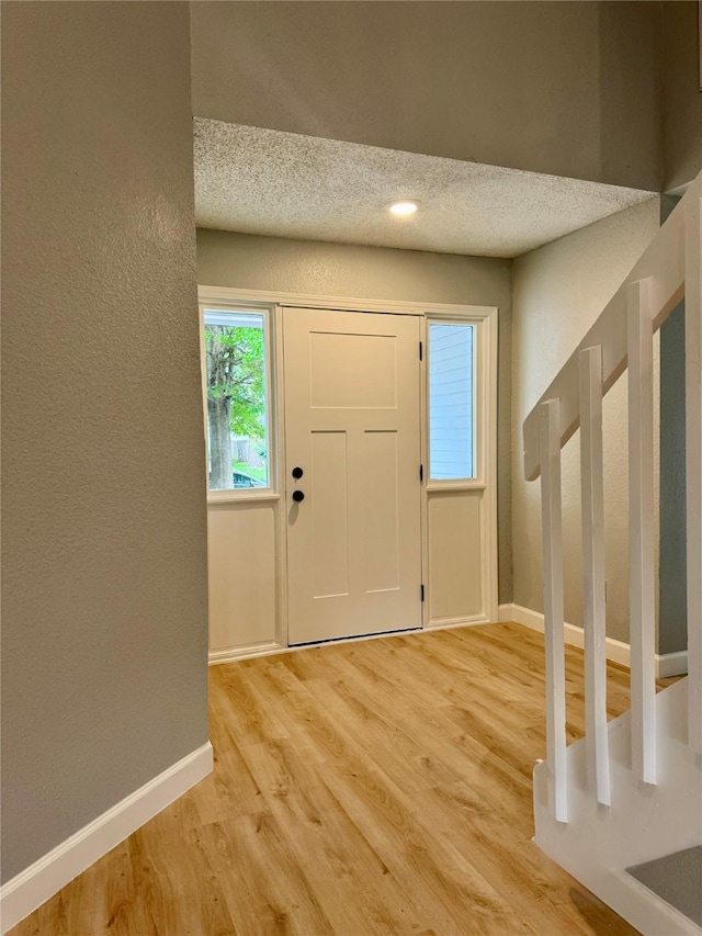 foyer entrance featuring baseboards, light wood-style flooring, a textured ceiling, and a textured wall